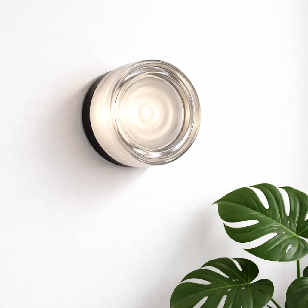 Applique murale cylindrique en verre transparent beige allumée sur mur blanc